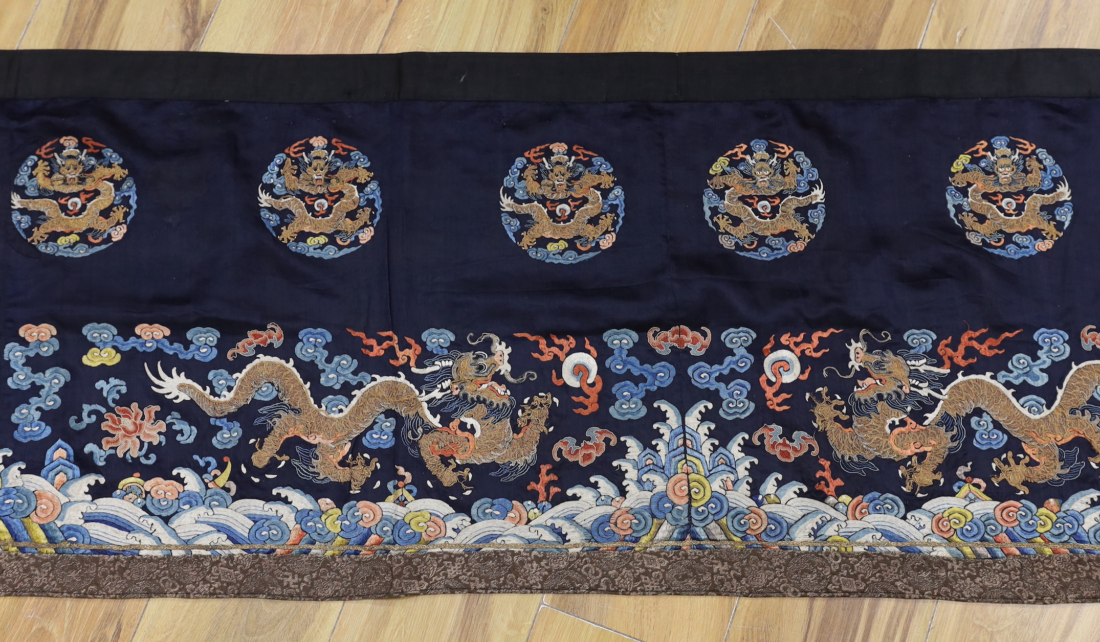 A Chinese long dark blue ground ‘dragon’ altar cloth, late Qing dynasty, polychrome embroidered, celestial dragons and mons amongst stylised clouds, 300 x 50cm